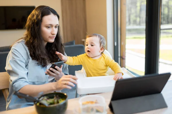 Vauva ja vanhemmat kiireinen digitaalinen vempaimia lounaan aikana kotona — kuvapankkivalokuva