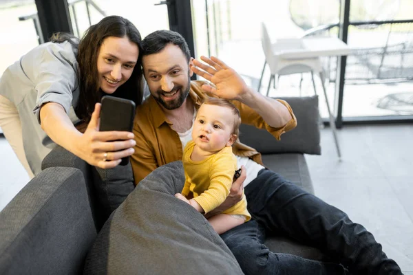 Šťastná rodina s jednoletým dítětem, které má videohovor na telefonu — Stock fotografie