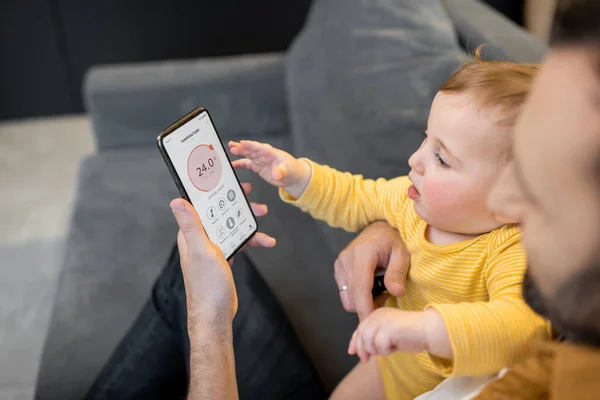Otec s dítětem ovládající domácí zařízení pomocí smartphonu — Stock fotografie