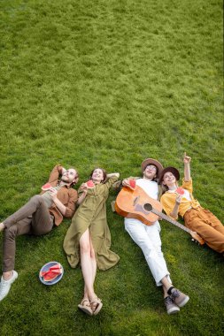 Dostlar yeşil çimlerde birlikte uzanır.