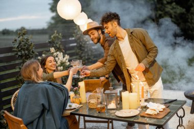 Genç arkadaşlar alacakaranlıkta kır evinin arka bahçesinde yemek yiyor.