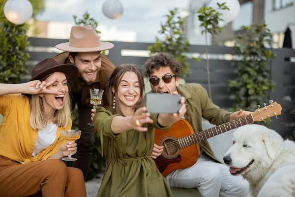 Amigos con bebidas y guitarra divirtiéndose en el patio trasero, llamando por teléfono —  Fotos de Stock