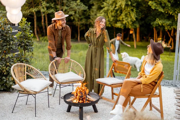 Friends sitting by a fireplace at backyard