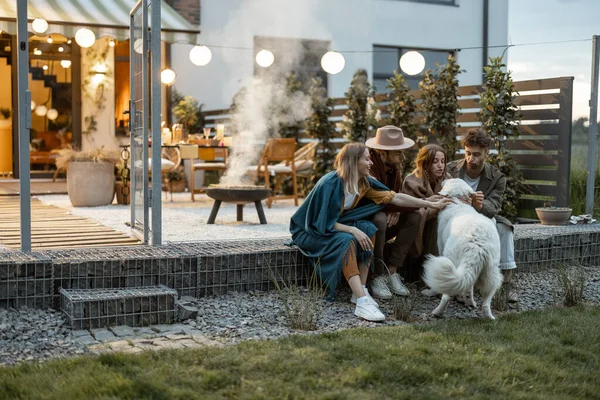 Amigos brincando com um cão perto da casa ao ar livre — Fotografia de Stock