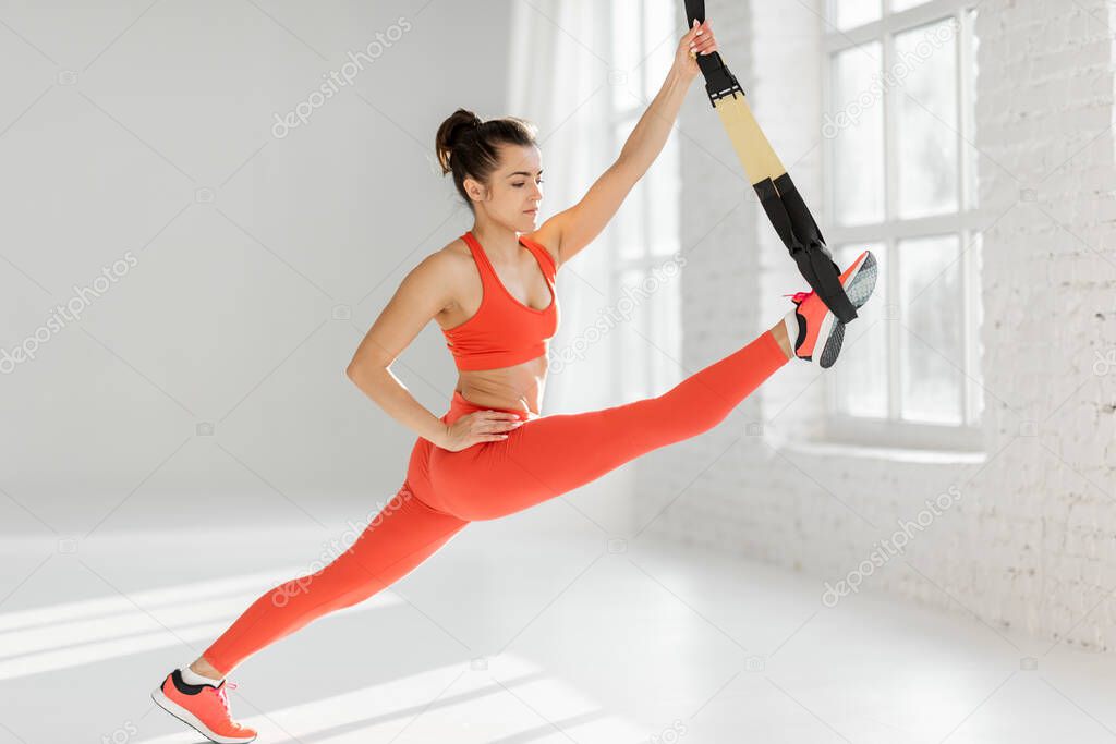 Athletic woman stretching with suspension straps at gym