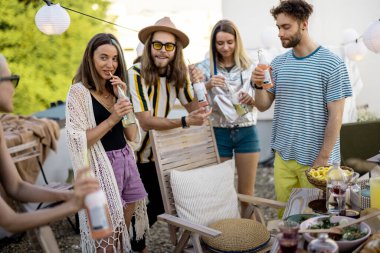 Genç şık arkadaşlar terasta şenlikli bir akşam yemeği yiyorlar.