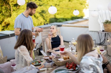 Genç şık arkadaşlar terasta şenlikli bir akşam yemeği yiyorlar.