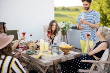 Genç şık arkadaşlar terasta şenlikli bir akşam yemeği yiyorlar.