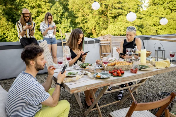 Människor tillbringar tid tillsammans, sitter separat i smarta telefoner på fest utomhus — Stockfoto