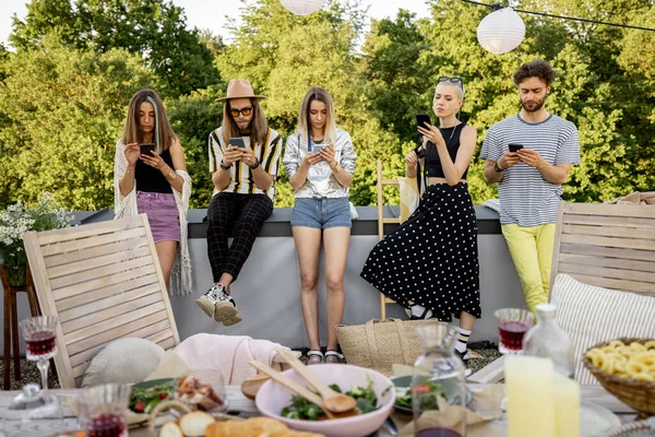 屋外のパーティーでスマートフォンに座って一緒に時間を過ごす人々 — ストック写真
