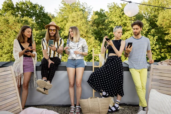 Människor tillbringar tid tillsammans, sitter separat i smarta telefoner på fest utomhus — Stockfoto