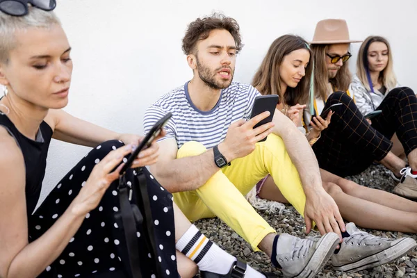 Přátelé sedící v řadě s chytrými telefony — Stock fotografie