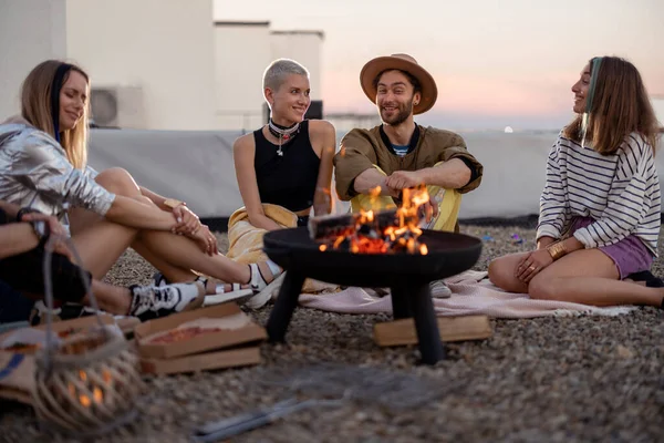 Vänner vid en öppen spis på taket vid solnedgången — Stockfoto