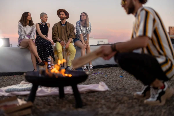 Friends by a fireplace on the rooftop at sunset — Stock Photo, Image