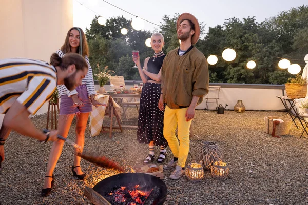 Amigos junto a una chimenea en la azotea al atardecer — Foto de Stock