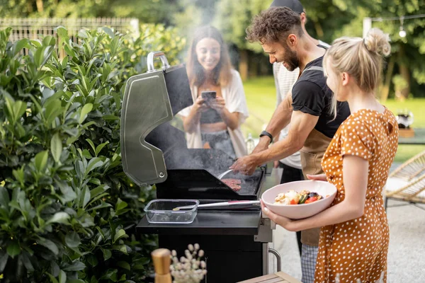 Gebeurt vrienden koken op een grill in de achtertuin — Stockfoto
