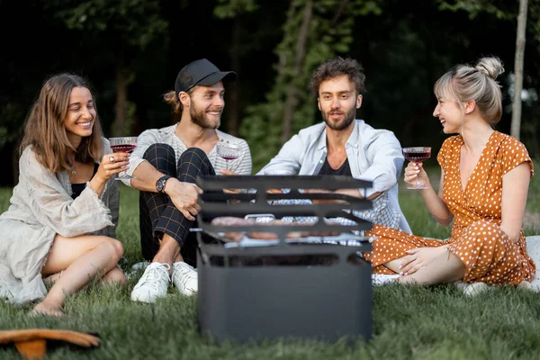 Amis assis ensemble au pique-nique avec barbecue et vin — Photo