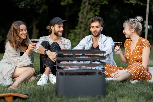 Amigos sentados juntos en el picnic con barbacoa y vino —  Fotos de Stock