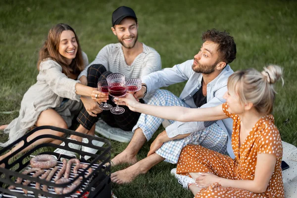 Друзья сидят вместе на пикнике с барбекю и вином — стоковое фото