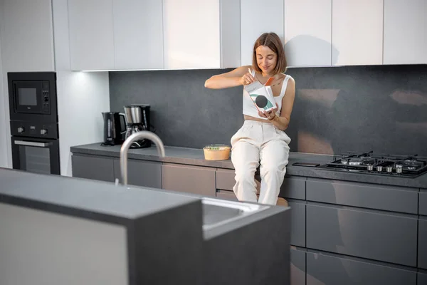 Frau isst Essen zum Mitnehmen im Sitzen in der modernen Küche — Stockfoto