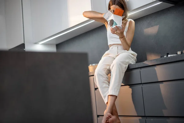 Frau isst Essen zum Mitnehmen im Sitzen in der modernen Küche — Stockfoto