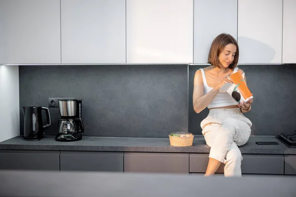 Frau isst Essen zum Mitnehmen im Sitzen in der modernen Küche — Stockfoto