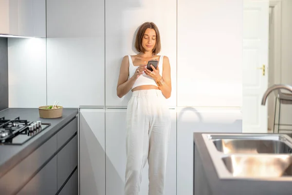 Mulher com telefone na cozinha moderna em casa — Fotografia de Stock