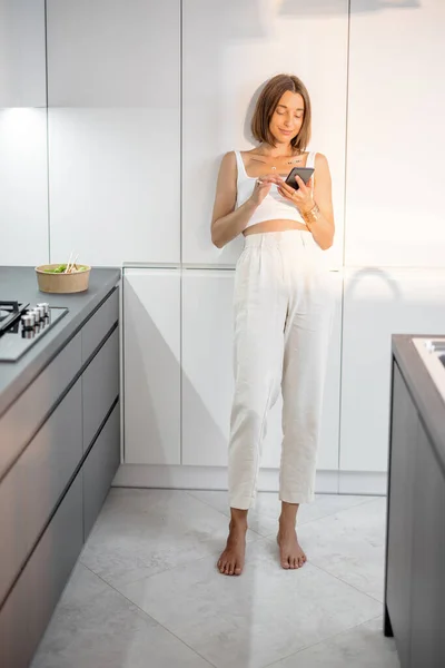 Vrouw met telefoon op de moderne keuken thuis — Stockfoto