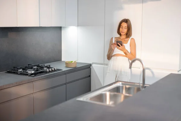 Kvinna med telefon på det moderna köket hemma — Stockfoto