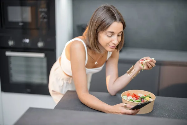 Vrouw met aziatische afhaalmaaltijden en smartphone in de keuken — Stockfoto