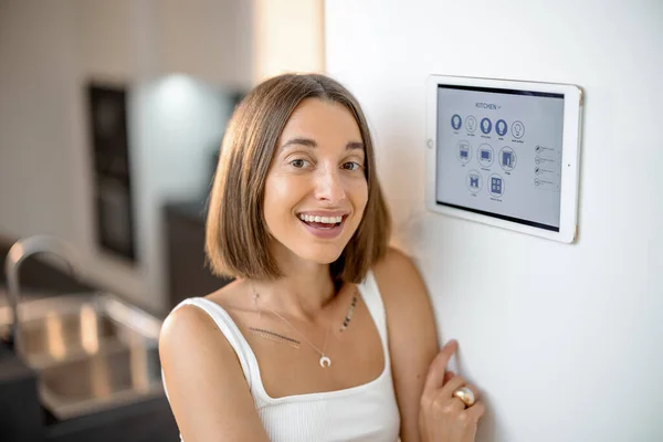 Glückliche Frau steuert intelligente Geräte mit Bedienfeld in der Küche — Stockfoto