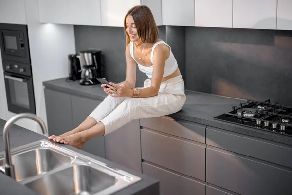 Žena s telefonem v moderní kuchyni — Stock fotografie