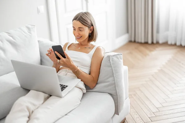 Žena pracuje s notebookem a telefonem na pohodlném gauči — Stock fotografie