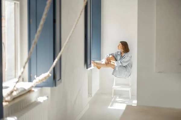 ผู้หญิงนั่งคนเดียวที่หน้าต่างที่บ้าน — ภาพถ่ายสต็อก