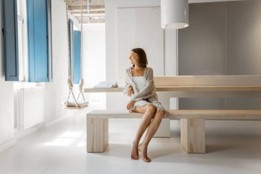 Modern bir stüdyo dairede rahatça oturan bir kadın.