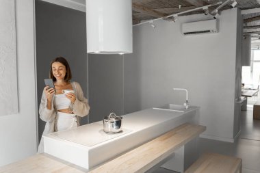 Modern mutfakta telefonu ve kahvesi olan bir kadın.