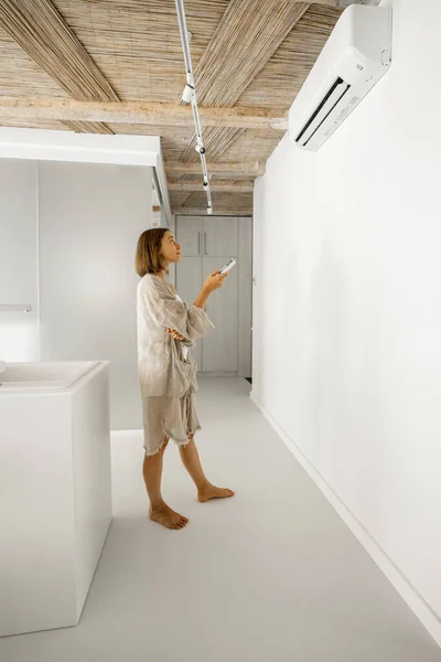 Kvinnan ställer in temperaturen på luftkonditioneringen hemma — Stockfoto