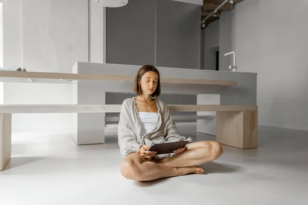 La mujer trabaja en una tableta digital mientras está sentada relajada en un apartamento moderno — Foto de Stock