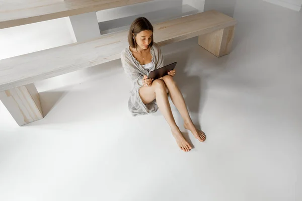 Mujer trabaja en una tableta digital mientras está sentada relajada en el suelo en casa — Foto de Stock