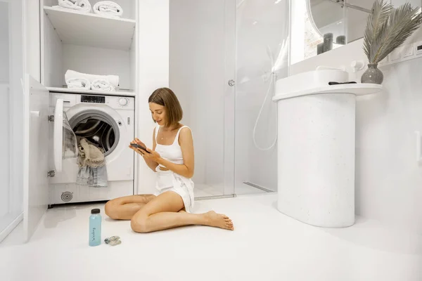 Femme avec téléphone cellulaire se préparant à laver les vêtements — Photo