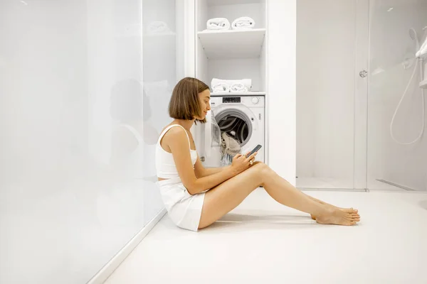 Vrouw met mobiele telefoon bereidt zich voor om kleren te wassen — Stockfoto