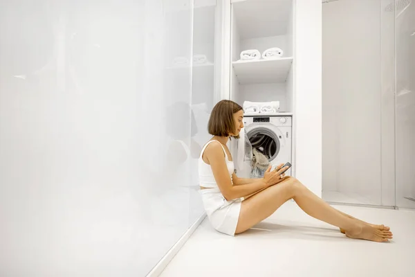 Kvinna med mobiltelefon förbereder sig för att tvätta kläder — Stockfoto
