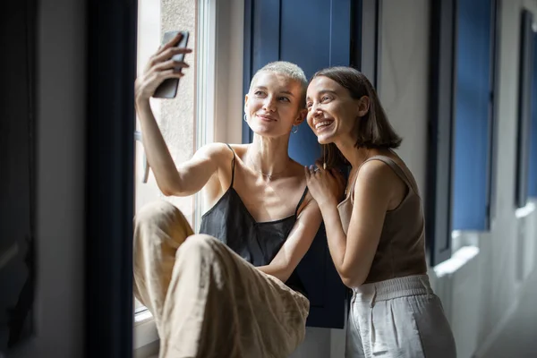 Dos mujeres se divierten, hablando en línea en el teléfono celular por la ventana —  Fotos de Stock