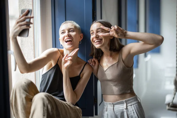 Dos mujeres se divierten, hablando en línea en el teléfono celular por la ventana —  Fotos de Stock