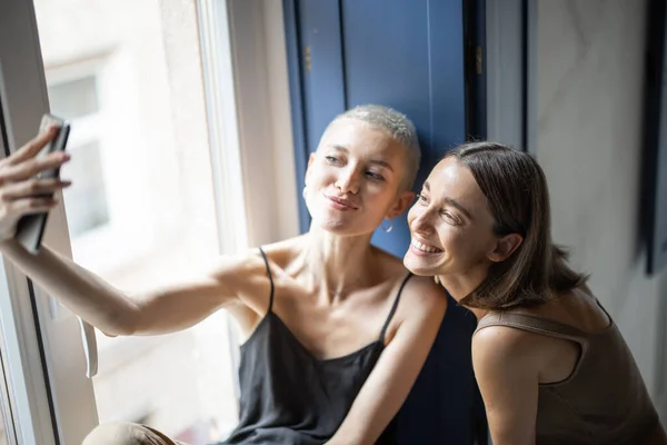 Twee vrouwen hebben plezier, praten online op mobiele telefoon door het raam — Stockfoto