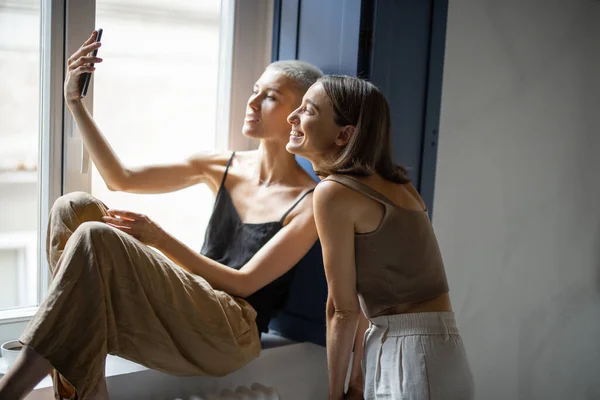 Dos mujeres se divierten, hablando en línea en el teléfono celular por la ventana — Foto de Stock