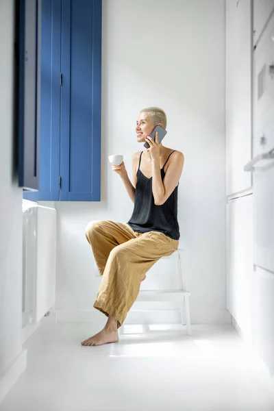 Donna con telefono e caffè vicino alla finestra a casa — Foto Stock