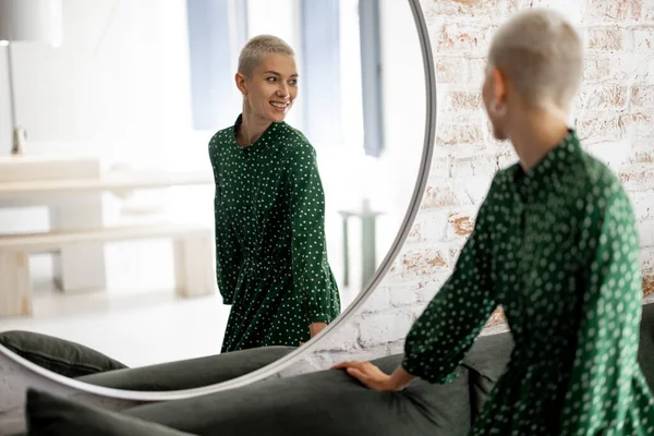 Mujer en vestido verde se mira a sí misma en el espejo en casa — Foto de Stock