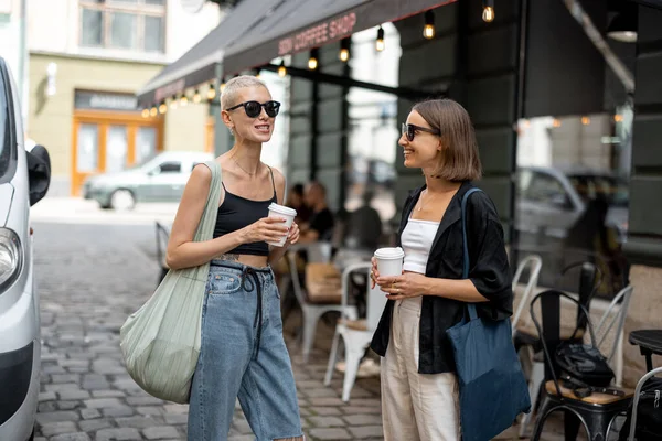 Elegante casal feminino de pé junto com uma xícaras de café ao ar livre — Fotografia de Stock