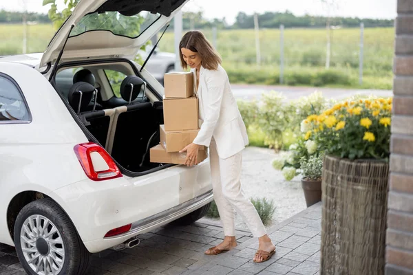 Žena vyzvedává balíčky z kufru auta poblíž domu — Stock fotografie